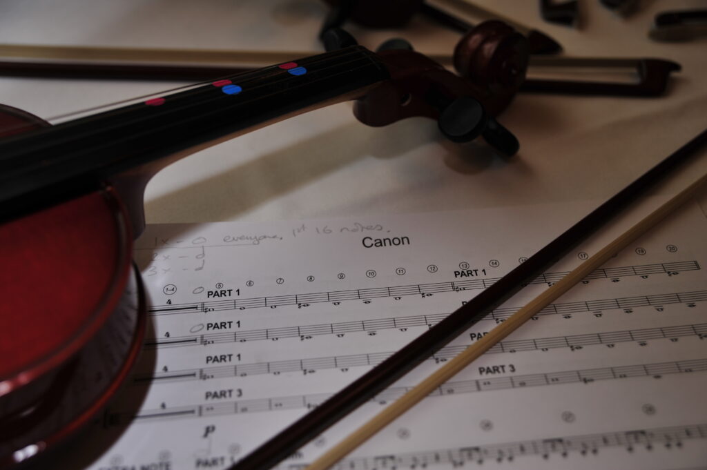 Close-up of a violin and bow resting on sheet music for Canon, showcasing the tools used during the Crescendo team building event.