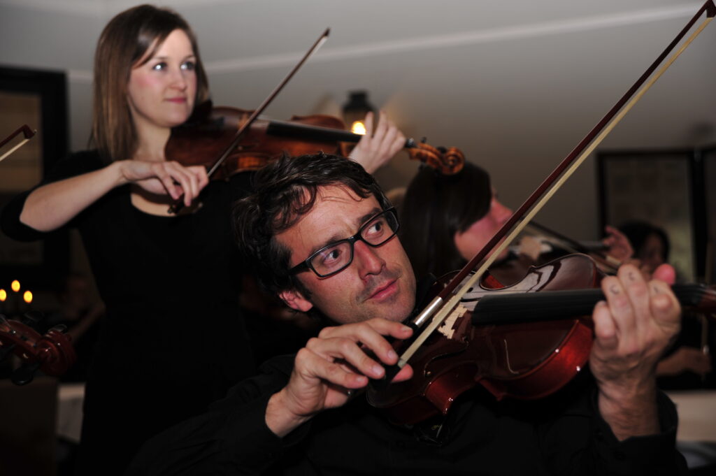 Focused participants playing violins together during the Crescendo team building event, showcasing collaboration and concentration through music.