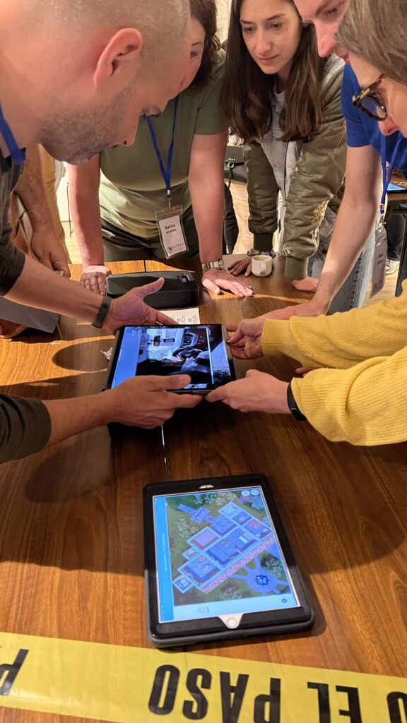 Participants in a 'Corporate CSI' team building event gather around a table, using iPads to examine digital evidence and clues as they work collaboratively to solve the mystery.