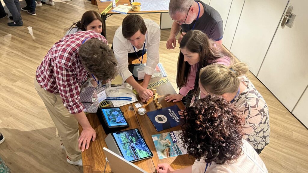 Participants in the 'Corporate CSI' team building challenge gather around a table, focused on solving clues from their detective briefcases and using digital tools to navigate a virtual crime scene.