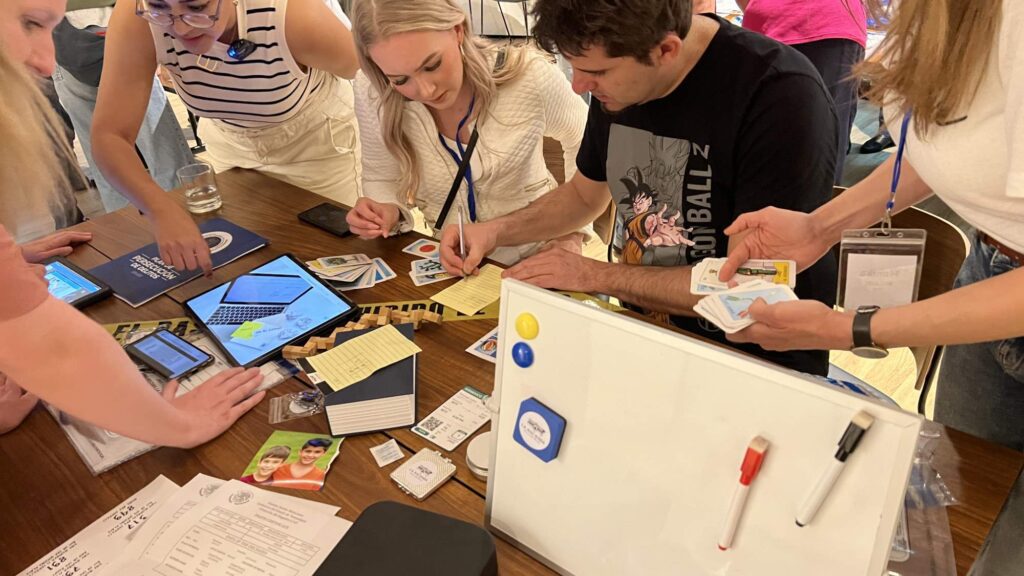 Team members actively engaged in solving a mystery during the 'Corporate CSI' team building event. Participants are examining evidence cards, taking notes, and using digital tools on tablets to analyze clues.