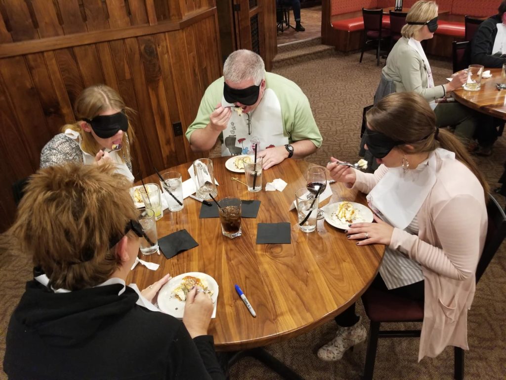 A group of participants at a Dining in the Dark team building event, engaging in a sensory dining experience while blindfolded.