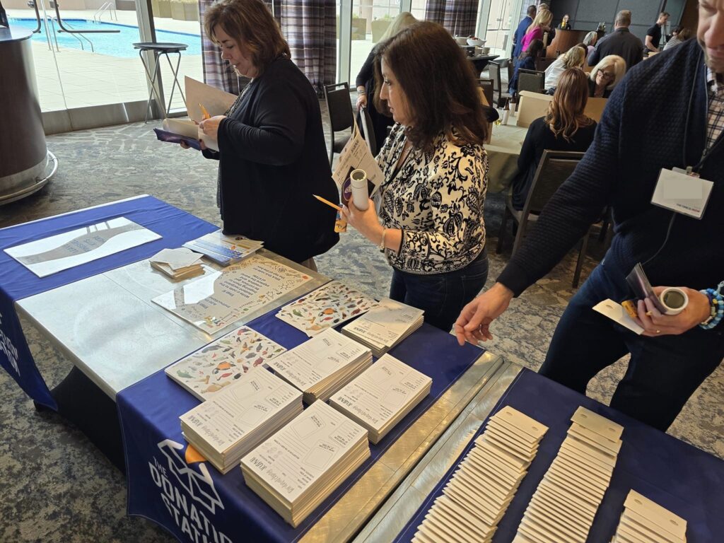 Participants organizing STEM activity kits on a table covered with The Donation Station banner during the Give the Gift of STEM corporate team building event'.