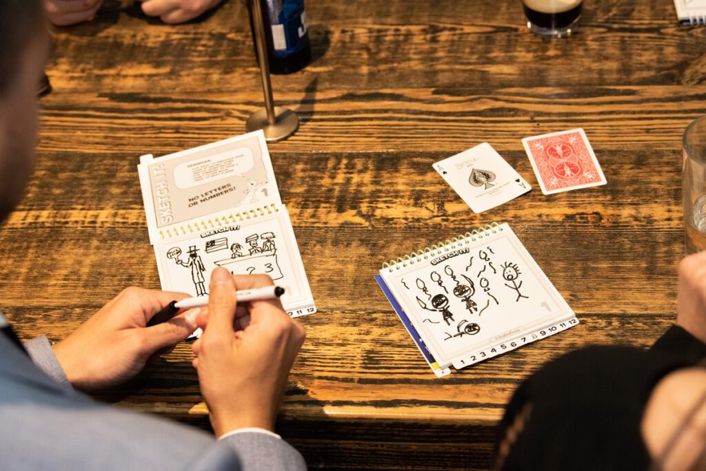 Team building participants engage in a creative drawing game during a business networking event, using cards and sketchpads to spark fun conversations and connections.