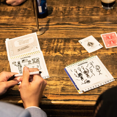 Team building participants engage in a creative drawing game during a business networking event, using cards and sketchpads to spark fun conversations and connections.