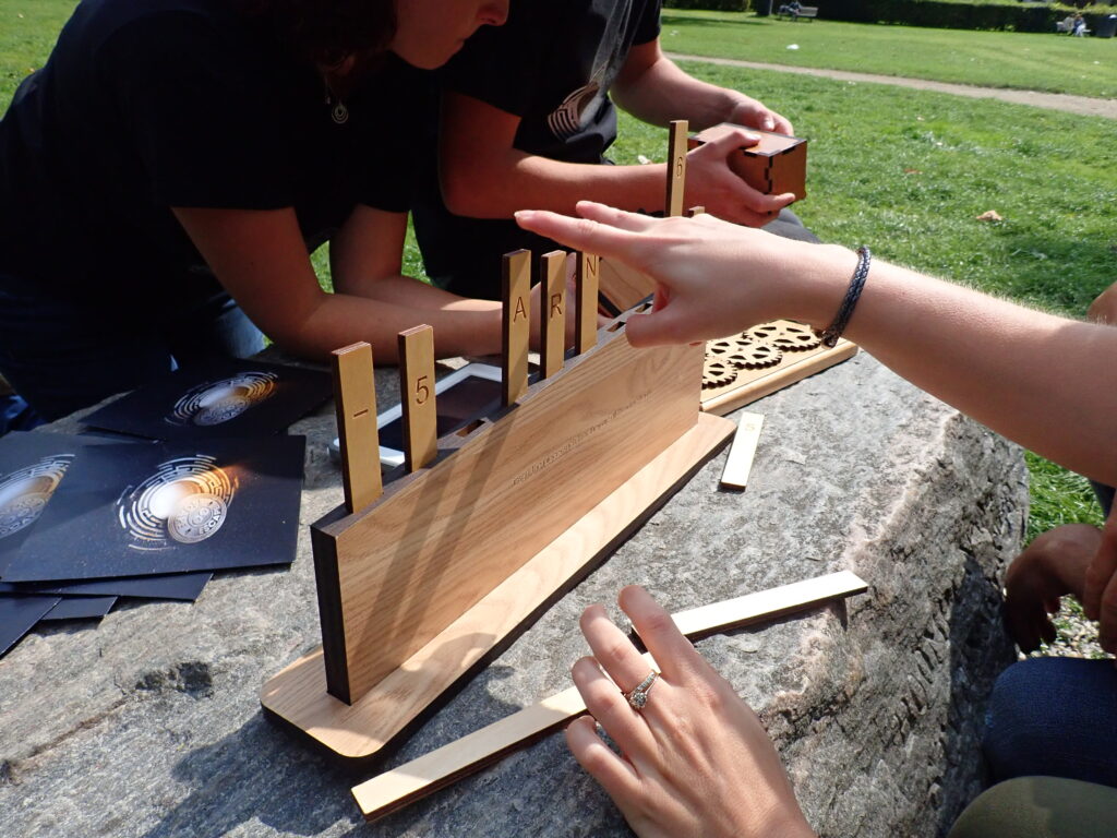 Close-up of team members interacting with a wooden puzzle as part of the 'Escape The Maze' team building event, emphasizing collaboration and problem-solving in an outdoor setting.