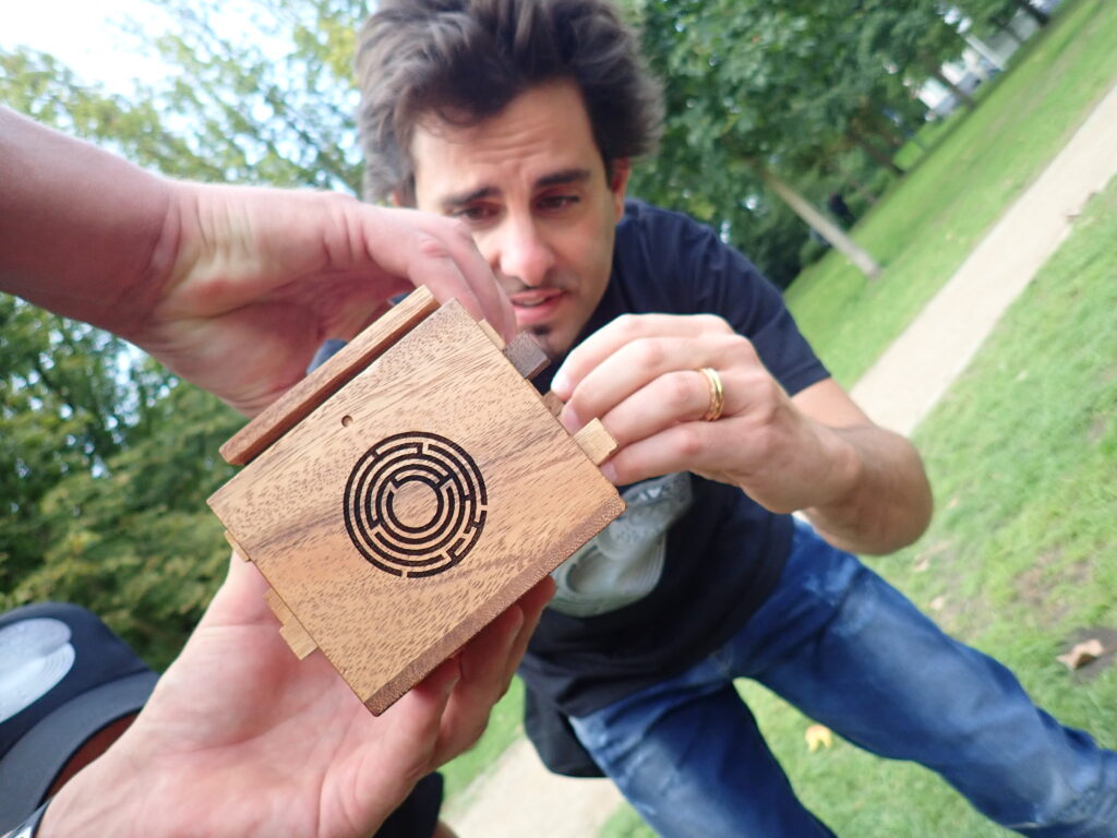 Participant carefully examines a small wooden puzzle box with a maze design during the 'Escape The Maze' team building event, focusing on solving the challenge.