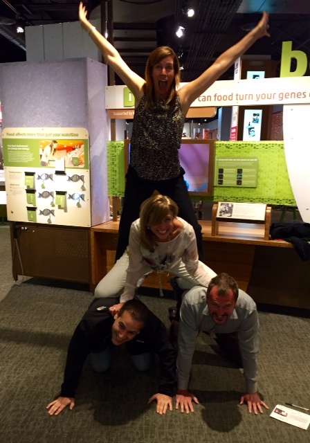 Team members forming a human pyramid during a museum scavenger hunt. This collaborative activity promotes teamwork, fun, and creativity while solving clues and engaging with interactive exhibits.