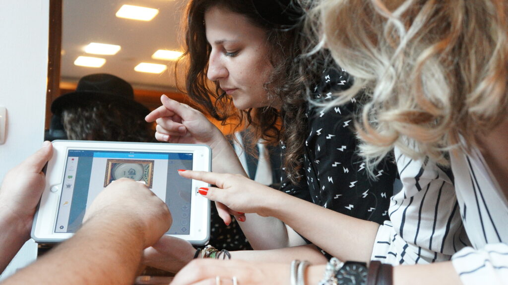 Three people closely examining a clue on a tablet screen during the 'Escape the Mob' team building activity. They are focused and engaged in solving a mystery, collaborating to piece together information and create a strategy for the game.