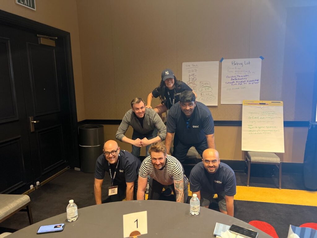 A group of participants in a team building event form a human pyramid indoors, smiling and working together.