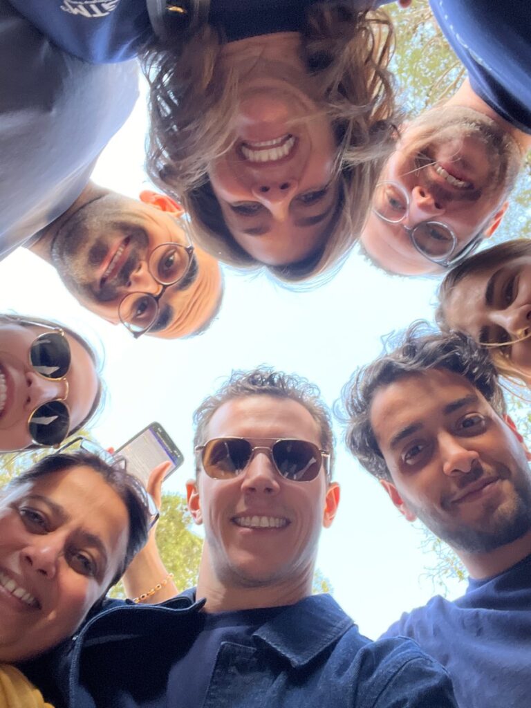 A group of smiling team members huddled in a circle, looking down at the camera during a fun and engaging outdoor team building activity.