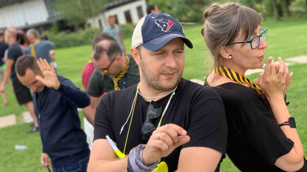 Outdoor team building challenge focused on trust and communication. Paired participants stand back-to-back, relying on non-verbal cues to complete the activity, reinforcing teamwork and cooperation.