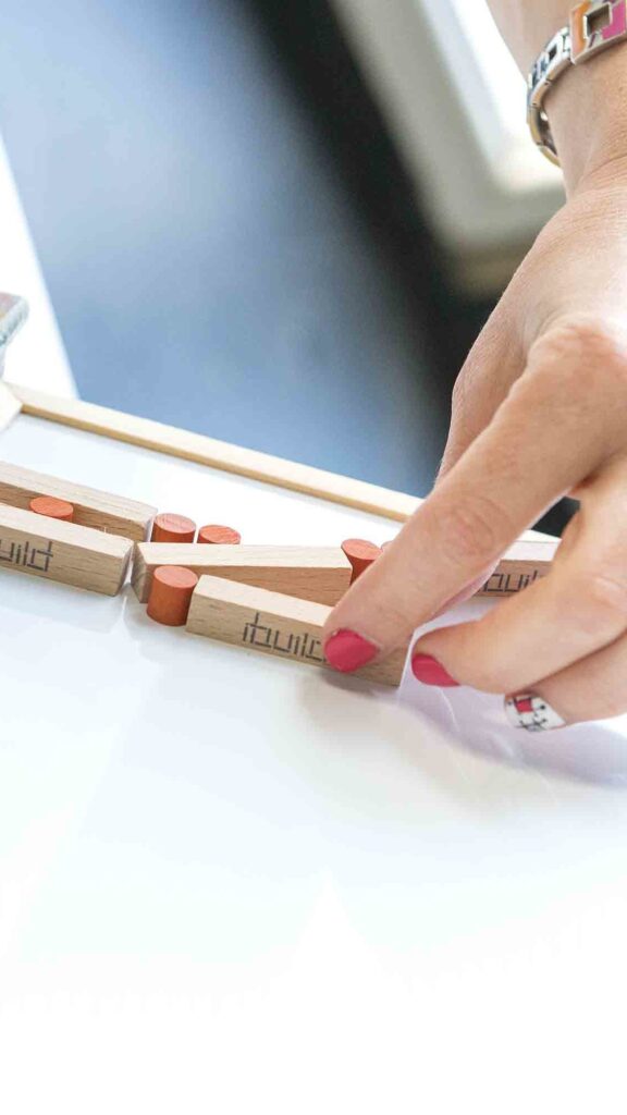 Close-up of a participant assembling an 'ibuild' model during a team building activity. The exercise emphasizes precision, communication, and collaboration to successfully recreate the structure.