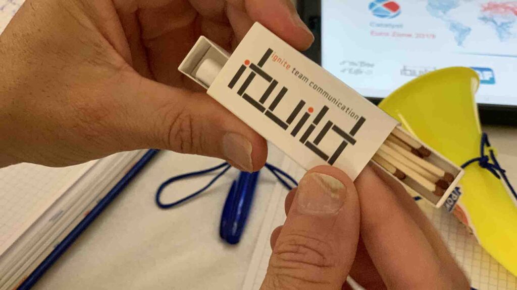 Close-up of an 'ibuild' matchbox, symbolizing the team building activity focused on communication and collaboration. The exercise challenges teams to convey instructions clearly for successful model replication.