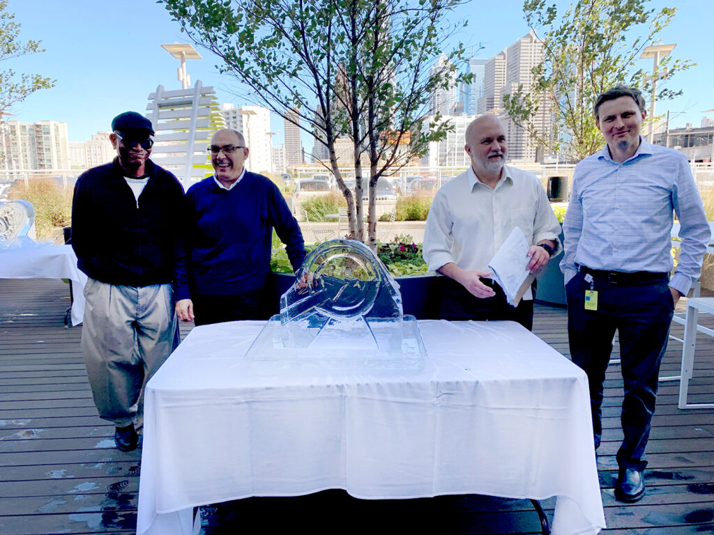 A group of participants proudly poses next to their completed ice sculpture, showcasing their teamwork and creativity during a Team building Ice Sculpting event.