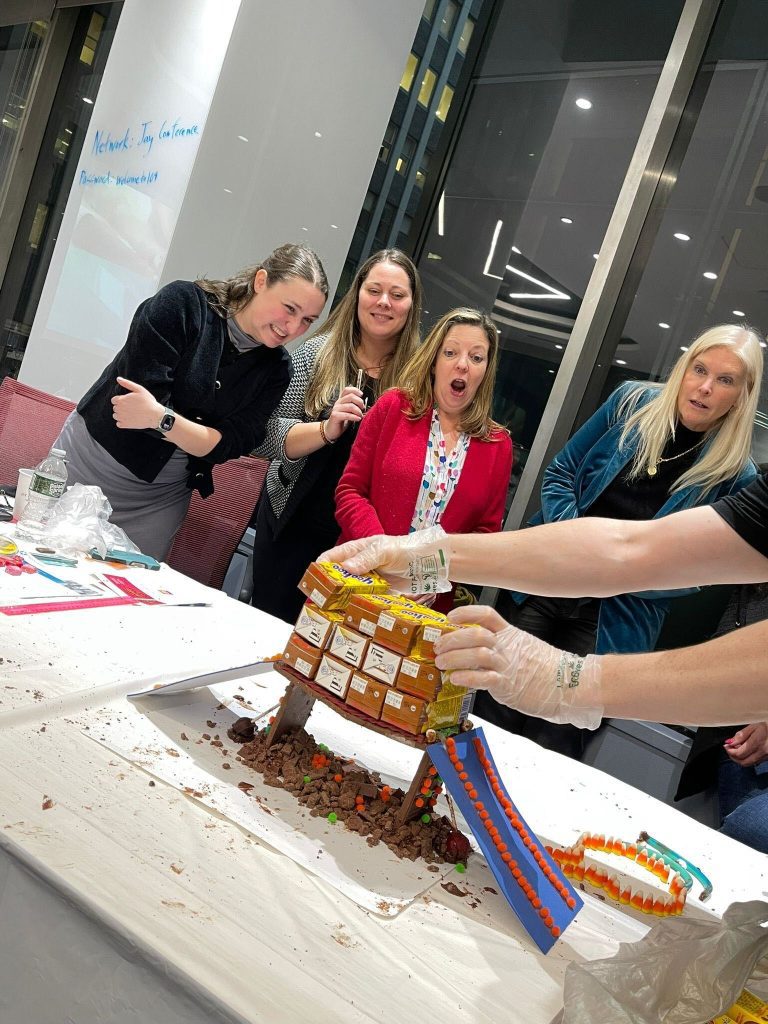 Participants in the Chocolate Challenge team building event express excitement as they successfully unveil their chocolate bridge structure, decorated with candies and icing.