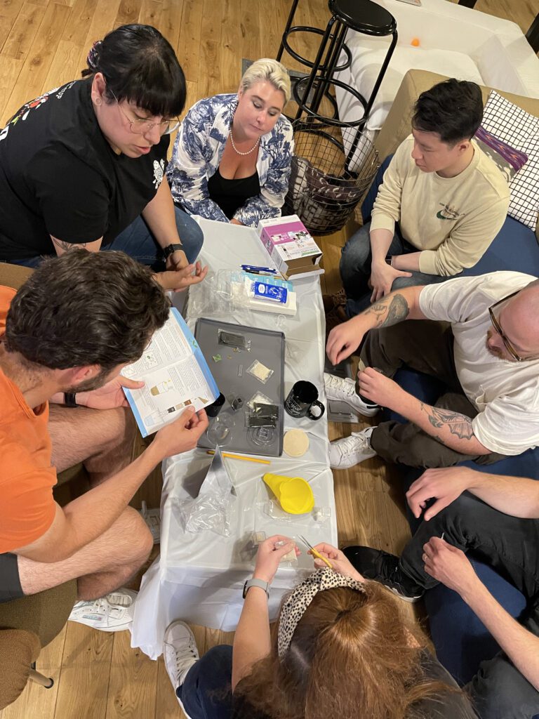 A small group of individuals work together to assemble water filtration kits during a Clean Water Connection event. The team follows instructions from a guide, engaging in a hands-on charitable team building activity.