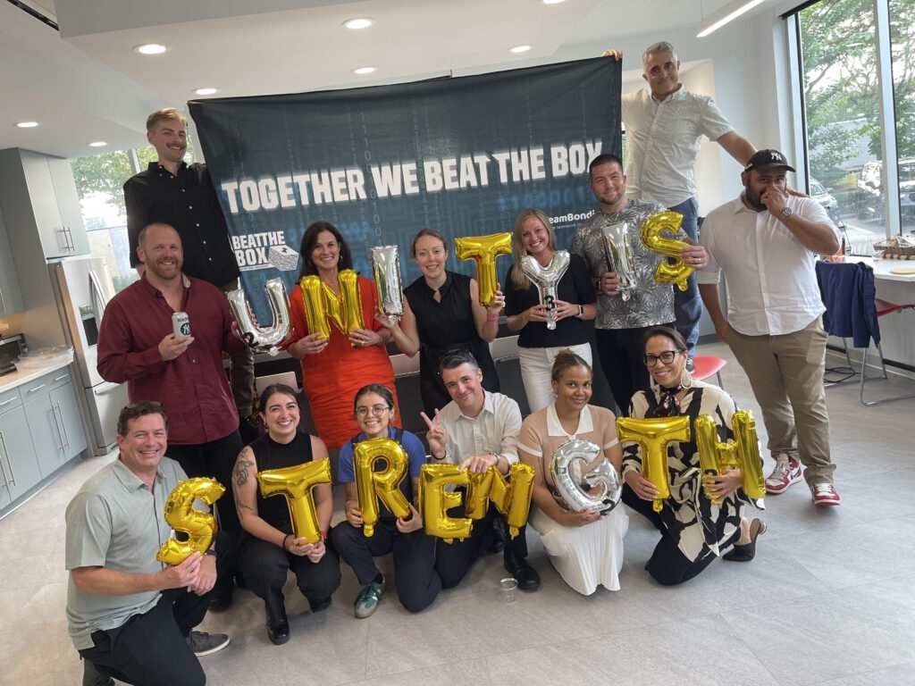 Team proudly displaying 'Unity is Strength' balloons after completing the Beat the Box team building event, celebrating their collaboration and shared achievement.