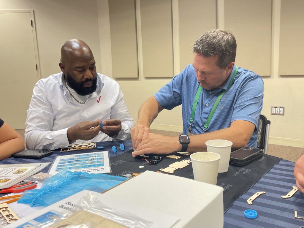 Two participants working together at a table to assemble components of a STEM project during the STEM Speedway team building activity, highlighting collaboration, problem-solving, and hands-on learning.