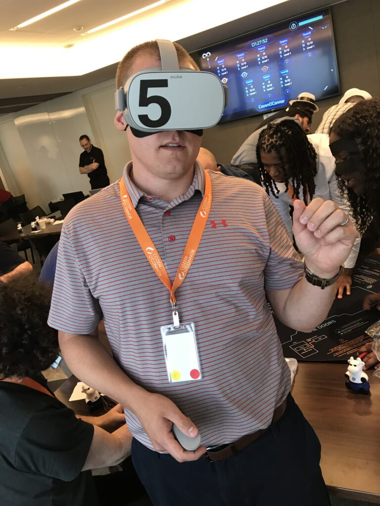 A participant wearing a VR headset labeled '5' engages in The Infinite Loop team building activity, immersing in a virtual reality experience during the event.