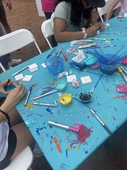 Participants painting small tiles at a table covered with art supplies during the Make-A-Mini-Mural activity at a corporate charitable team building event called 'the Donation Station'.