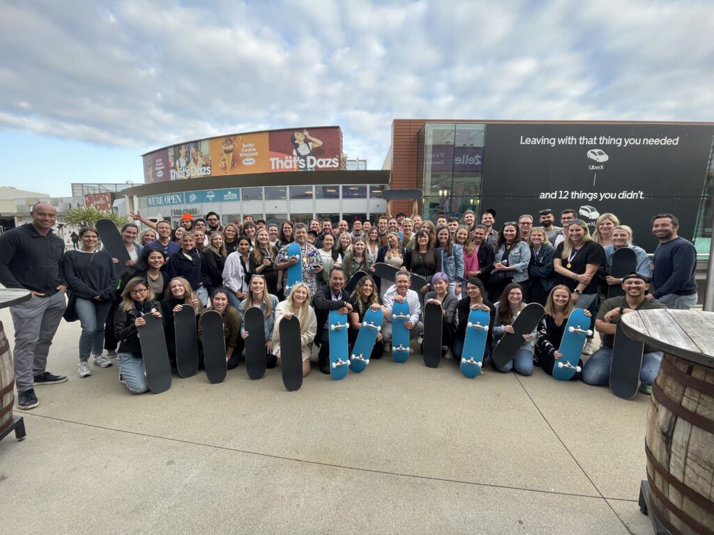 Large group of participants proudly display skateboards they built together during The Mystery Bus team building event, fostering teamwork and creativity.