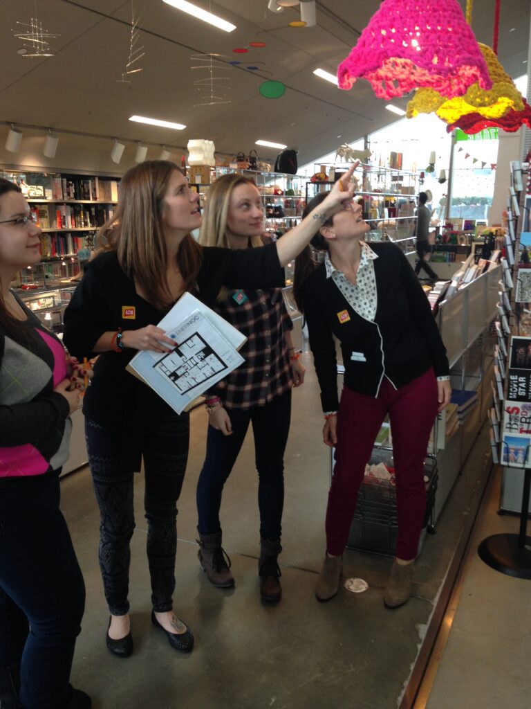 Team members collaborating during a museum scavenger hunt, engaging with a colorful art piece while solving clues. The activity fosters teamwork, creativity, and exploration in an interactive setting.