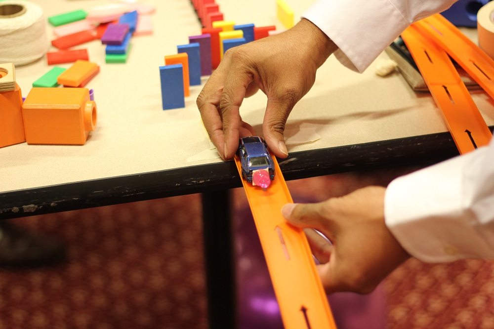 Close-up of a participant placing a toy car on a track as part of a hands-on activity during the Domino Effect team building event.