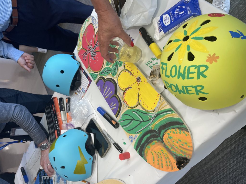 Vibrantly painted skateboard and helmets created during a charitable team building event. Participants worked together to design and assemble skate gear for donation, promoting teamwork, creativity, and community impact.