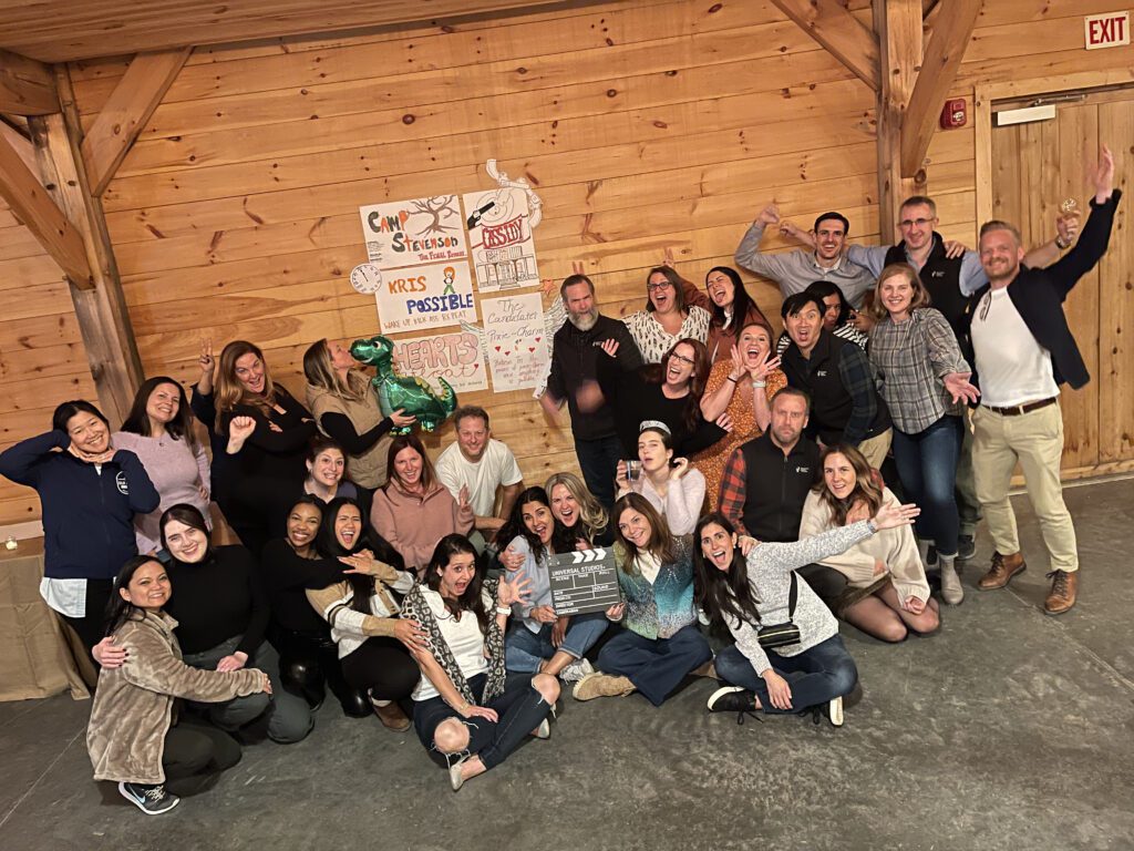 A large group of participants poses enthusiastically in front of handmade posters during a film festival movie making team building event.