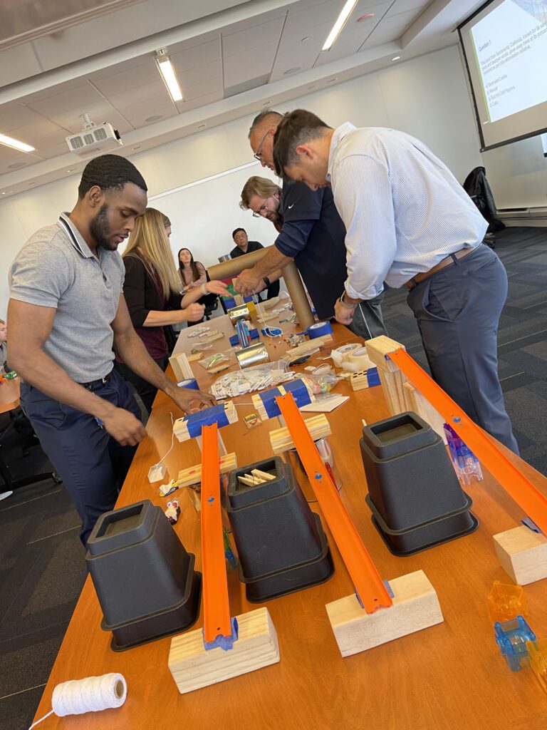 Team members collaborating during the Domino Effect team building event, working with various materials and components on a table to create complex contraptions.