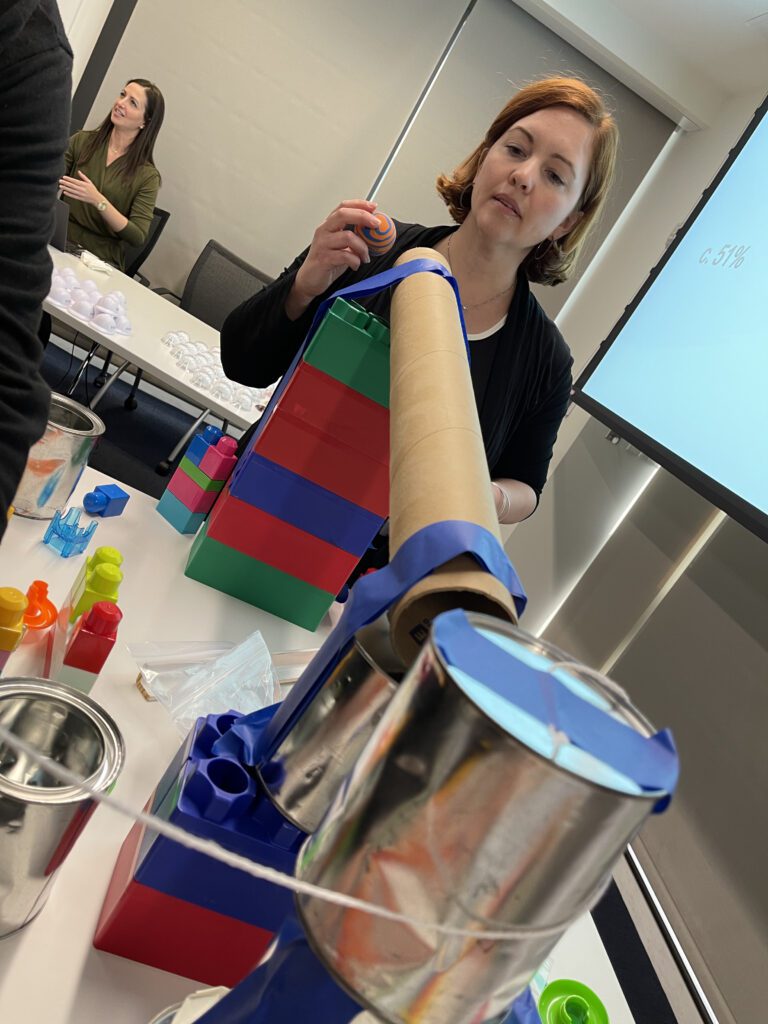 Team member constructing a creative contraption during the Domino Effect team building event, focusing on building a structure with colorful materials.