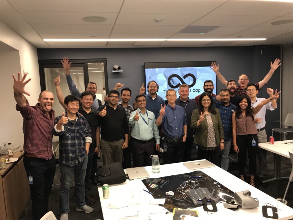 A group of participants enthusiastically pose with raised hands at the conclusion of The Infinite Loop team building event.