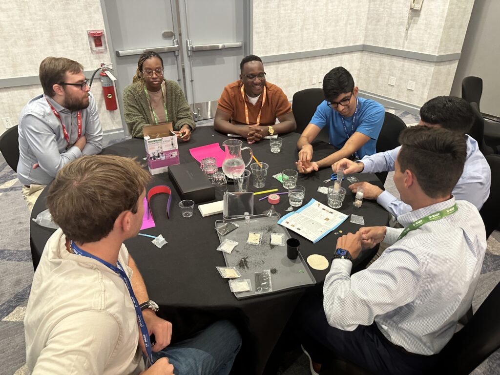 A group of professionals gather around a table, collaborating on assembling water filtration kits during a Clean Water Connection team building event. The team works together on this interactive project, learning about the global water crisis and the impact of providing clean water to communities in need. The activity fosters teamwork and raises awareness of clean water challenges around the world.