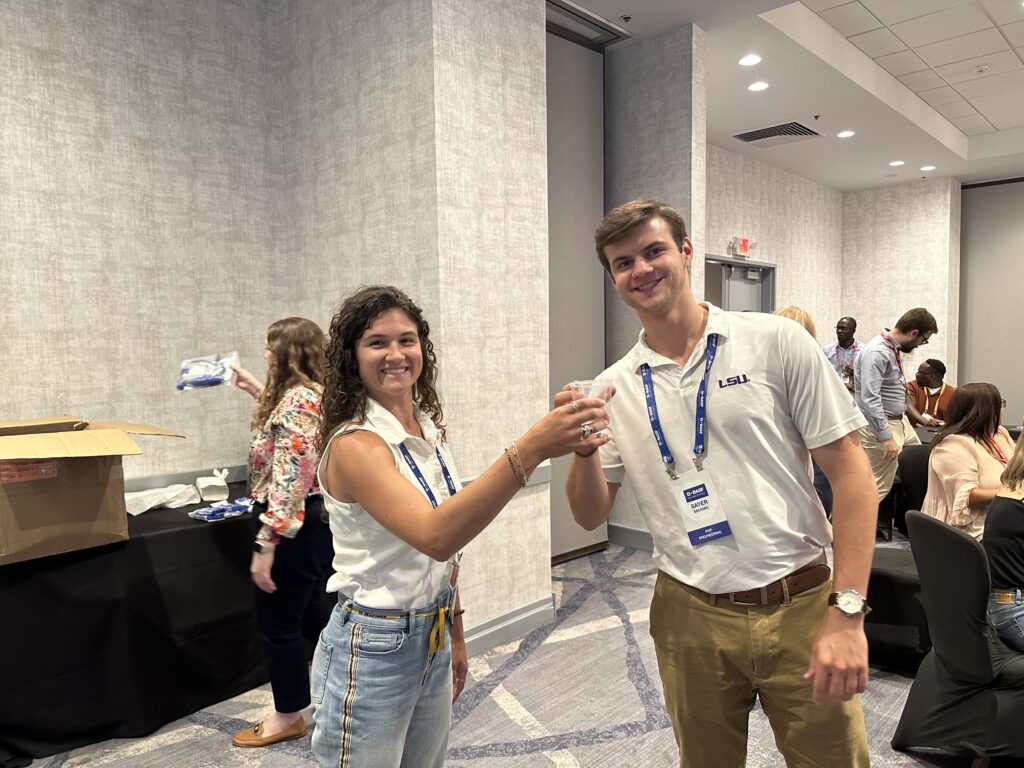 Two smiling participants at a Clean Water Connection event raise glasses of clean water, celebrating the successful assembly of a water filtration kit. The team building activity fosters teamwork and raises awareness about the importance of providing clean water to communities in need.