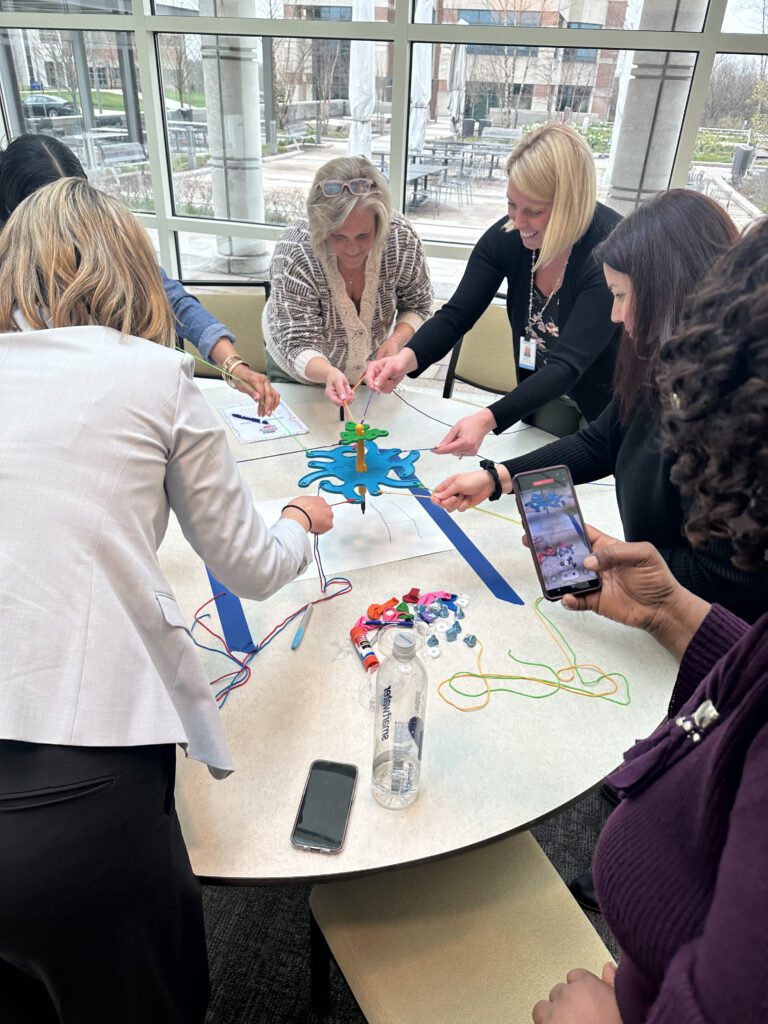 A group of women are gathered around a table, working together on a team building activity called 