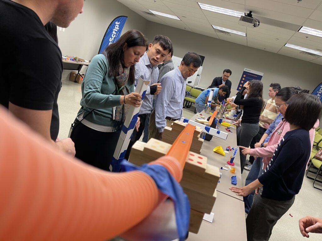 Teams working together to build an intricate Rube Goldberg machine during the Domino Effect team building activity.