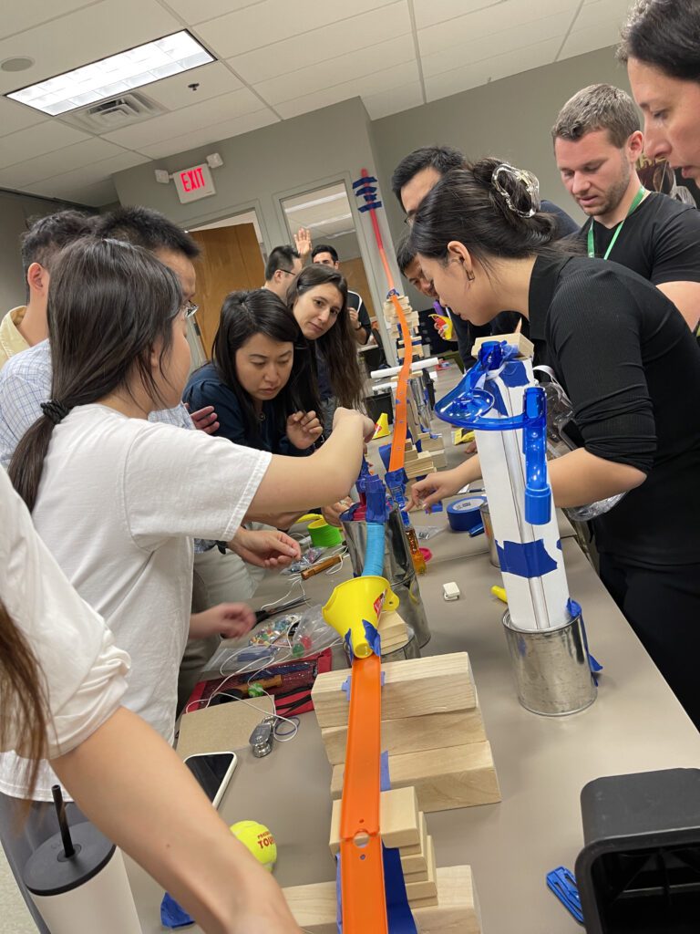 A group of participants collaborates to assemble a complex chain reaction during the Domino Effect team building activity, focusing on constructing innovative contraptions.