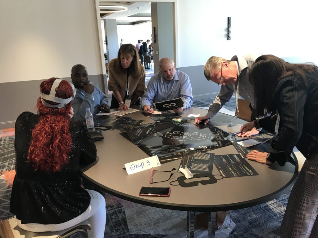 A group of participants collaborating on puzzle tasks at The Infinite Loop team building event, while one team member wears a VR headset to solve virtual challenges.