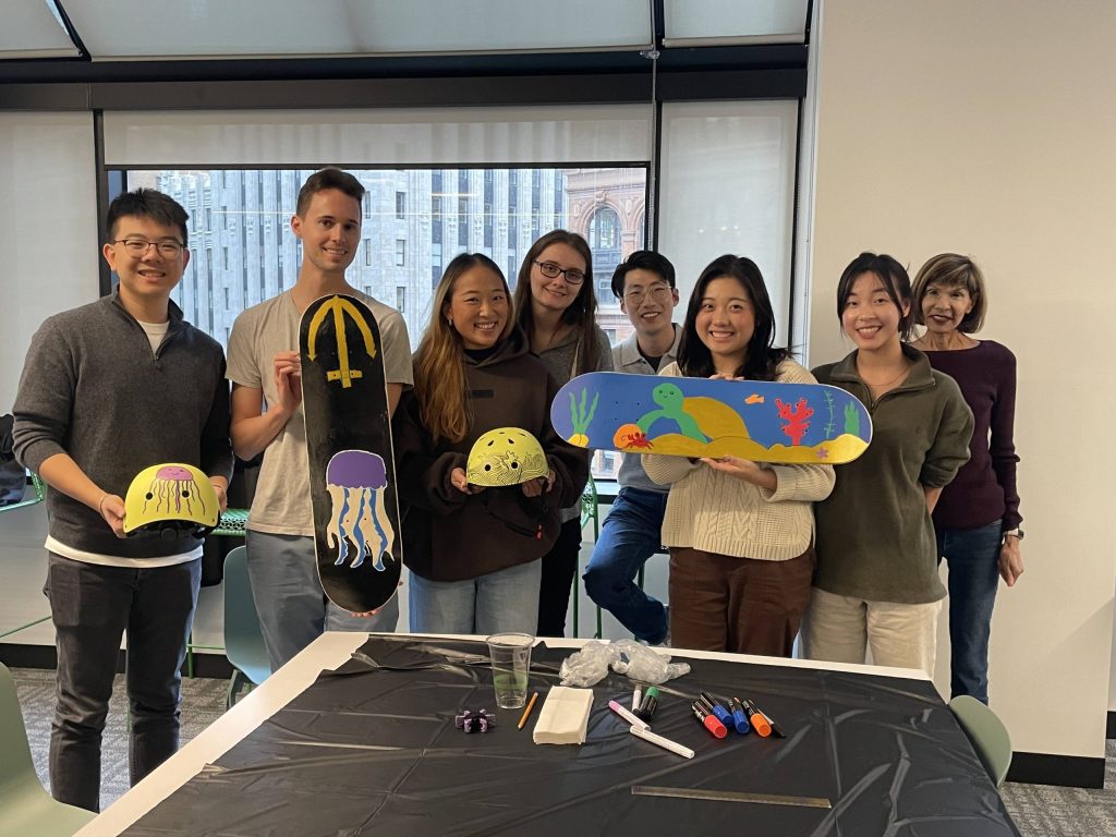 Team showcasing their hand-painted skateboards and helmets during a charitable team building event. Participants collaborated to design and assemble skate gear for donation, fostering creativity, teamwork, and community giving.