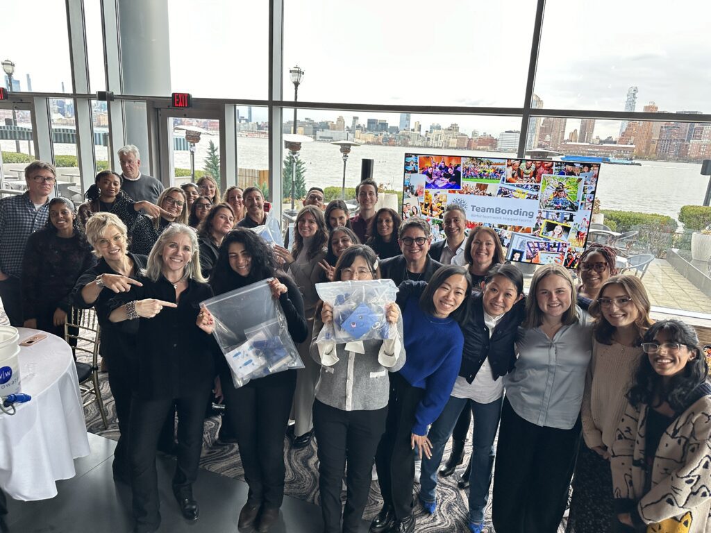 A large group of participants at a Clean Water Connection team building event proudly display completed water filtration kits. The group celebrates their collaborative effort in assembling filtration kits that will provide clean water to communities in need.