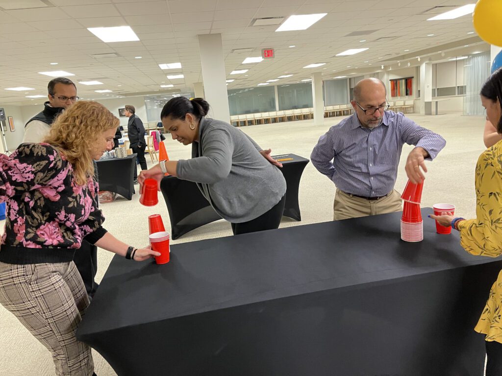 Participants concentrating on a cup stacking challenge during the In It to Win It team building activity, showcasing coordination, speed, and competitive spirit in a collaborative setting.