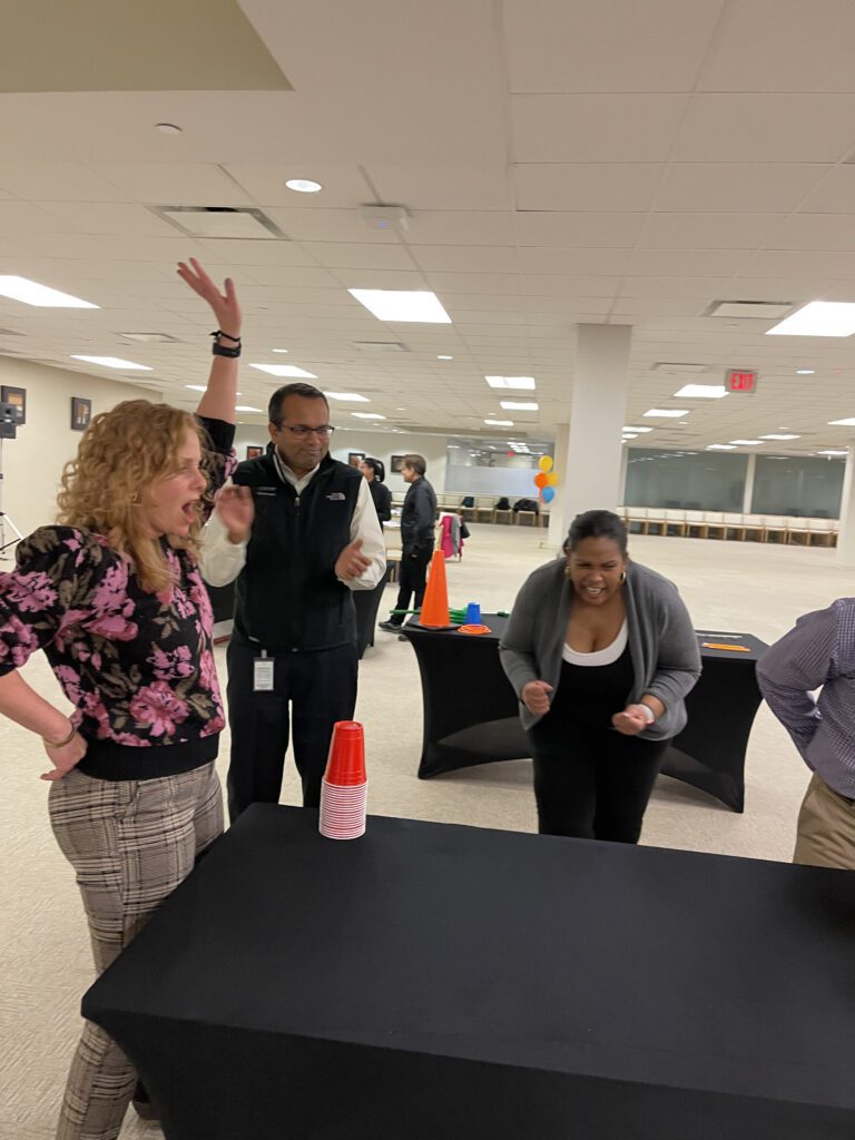 Participants enthusiastically reacting and cheering during a cup stacking challenge in the In It to Win It team building game, displaying excitement, competitive spirit, and teamwork.