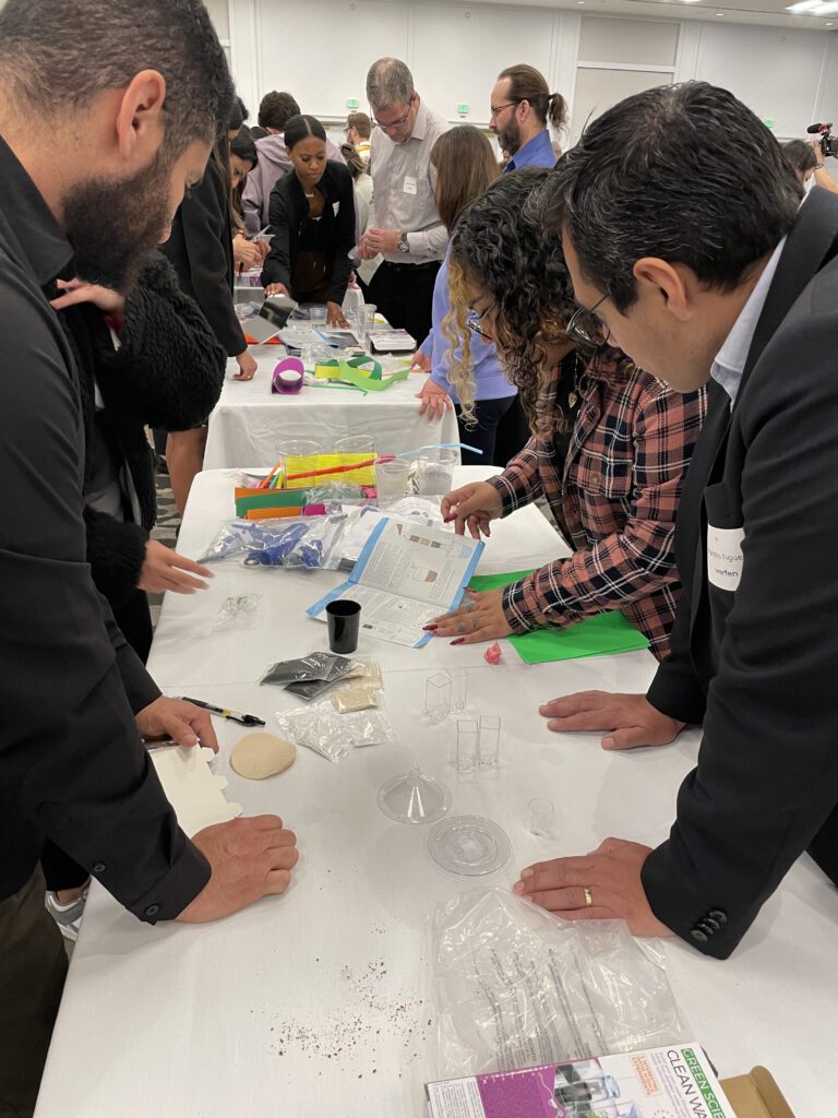 Participants at a Clean Water Connection event collaborate on assembling water filtration kits, carefully following instructions laid out on the table. The activity engages individuals in hands-on learning about the global water crisis and how filtration systems can provide clean water to underserved communities. The team building event fosters teamwork and practical education on the importance of clean water access.