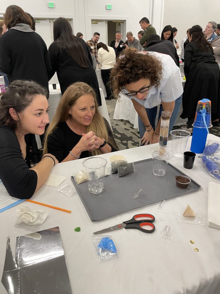 Three participants at a Clean Water Connection team building event closely observe their water filtration assembly in progress. The hands-on activity allows them to understand how filtration systems work and the importance of clean water access.