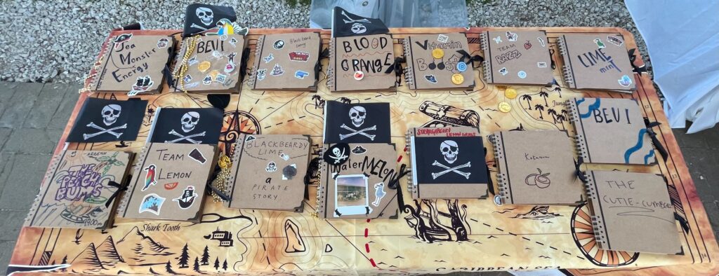 A table filled with pirate-themed notebooks decorated with stickers, skulls, and team names during a Custom Team Building event. The creative decorations reflect the playful pirate theme of the event.