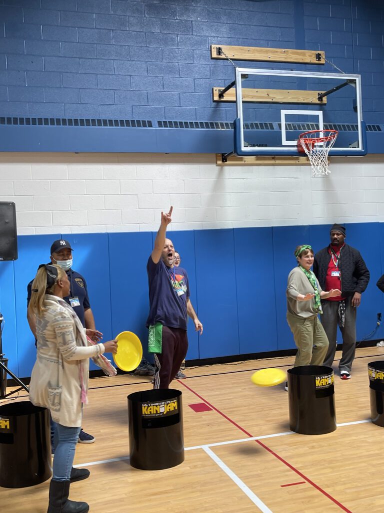 There's a group of people inside a gymnasium engaged in a team building activity. One participant appears to be enthusiastically celebrating or signaling success, adding a lively and energetic atmosphere to the scene.