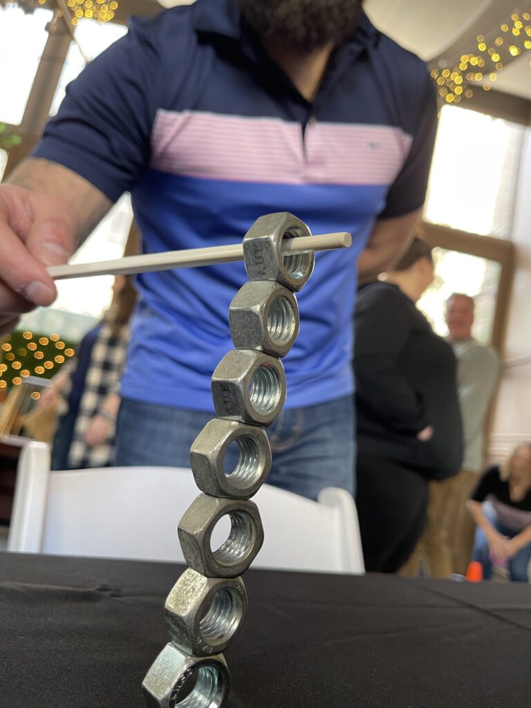 A close-up of a participant carefully balancing metal nuts on a table using a chopstick during the In It to Win It team building challenge, demonstrating precision, focus, and steady hands.