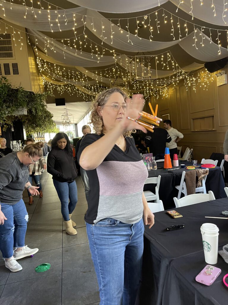 A participant engaged in a pencil flipping challenge during the In It to Win It team building game, focusing intently while attempting to catch multiple pencils in one hand, showcasing coordination and agility.