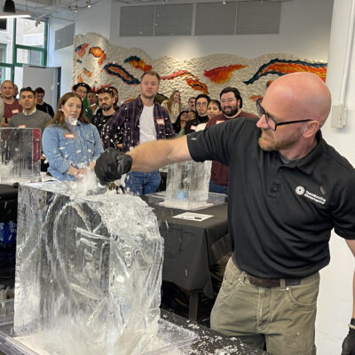 A facilitator demonstrating ice sculpting techniques while participants watch during a Team building Ice Sculpting workshop, encouraging collaboration and skill development.